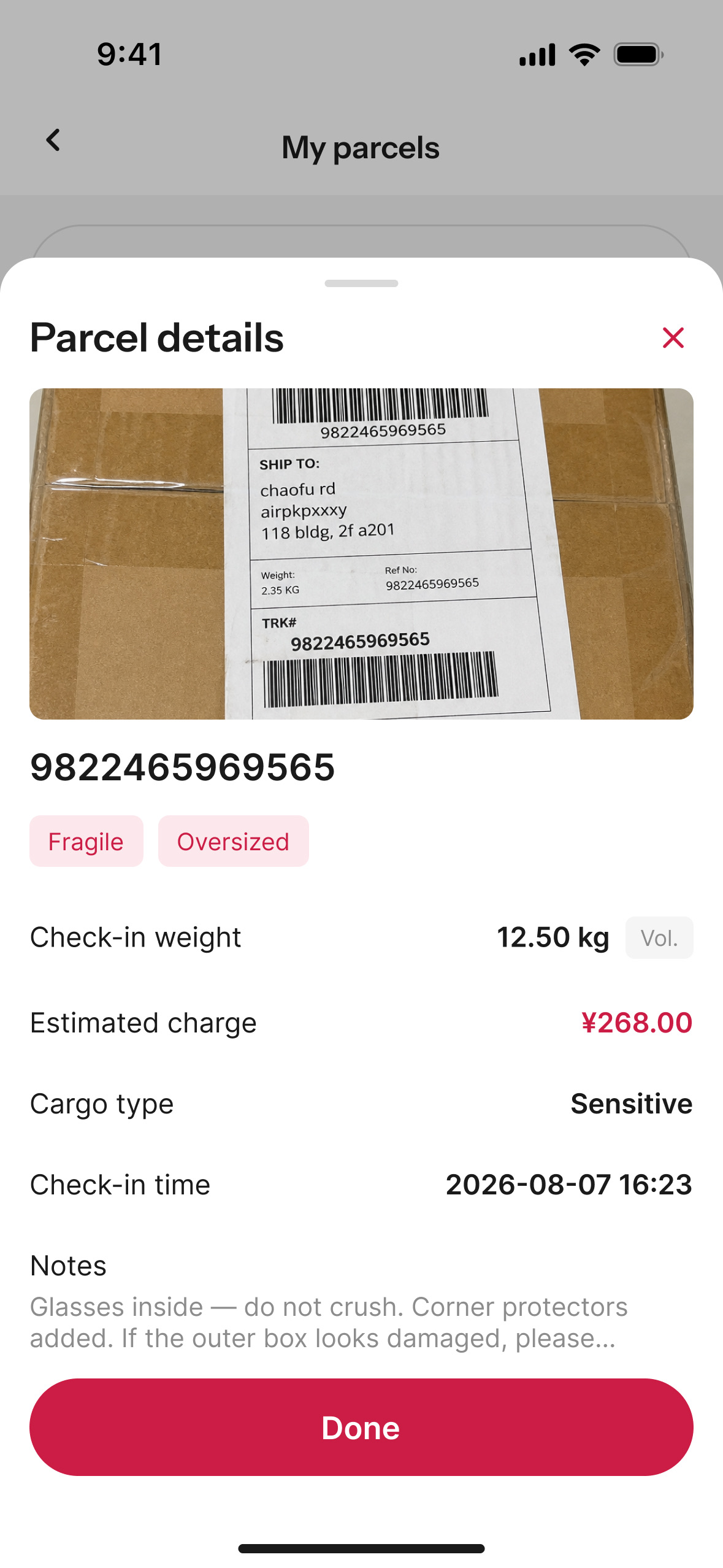The parcel back in the buyer's app: the warehouse's own photograph of the package, its printed label carrying the air-freight code AIRPKPXXXY inside the street address. Below it the tracking number, tags reading fragile and oversized, a check-in weight of 12.50 kg marked volumetric, an estimated charge of 268 yuan, the cargo type, the check-in time, and the buyer's own note — glasses inside, do not crush, corner protectors added.